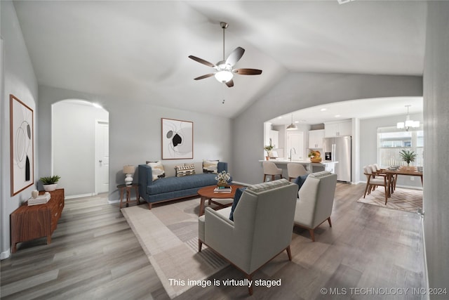 living room featuring ceiling fan with notable chandelier, light hardwood / wood-style floors, vaulted ceiling, and sink