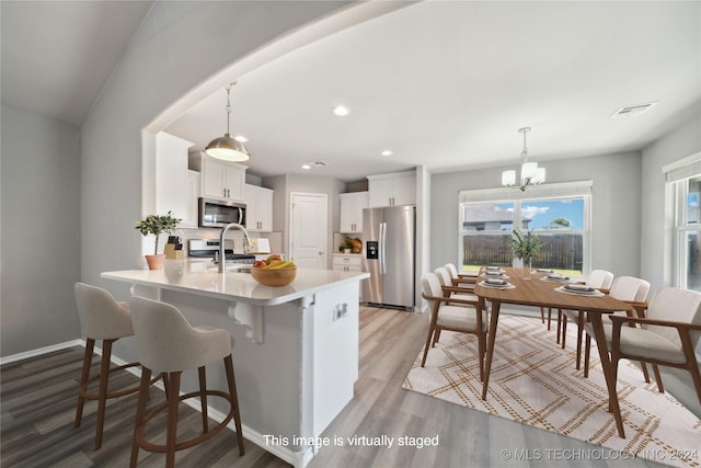 kitchen featuring hanging light fixtures, white cabinetry, appliances with stainless steel finishes, light hardwood / wood-style floors, and kitchen peninsula