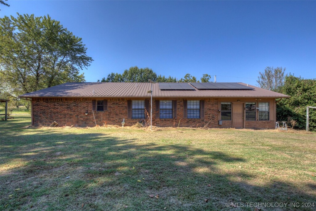 111 N T 200 St, Stigler, OK 74462 - rear view of property featuring solar panels, a lawn, brick siding, and metal roof