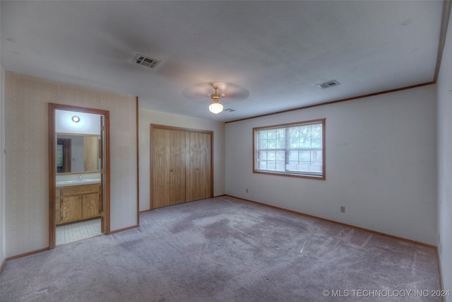 unfurnished bedroom featuring a closet, light carpet, ensuite bath, sink, and ceiling fan