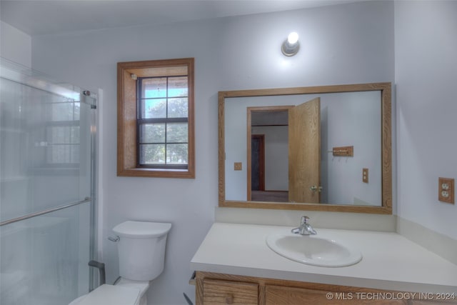 bathroom featuring toilet, a shower with shower door, and vanity