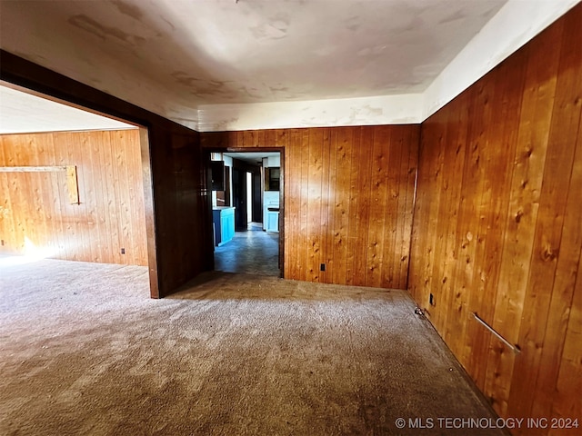 unfurnished room featuring wooden walls and dark colored carpet