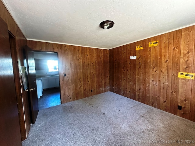 spare room with dark carpet, wooden walls, and a textured ceiling