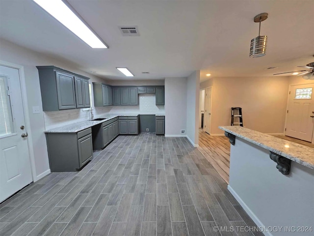 kitchen featuring light stone counters, hanging light fixtures, sink, gray cabinetry, and hardwood / wood-style floors