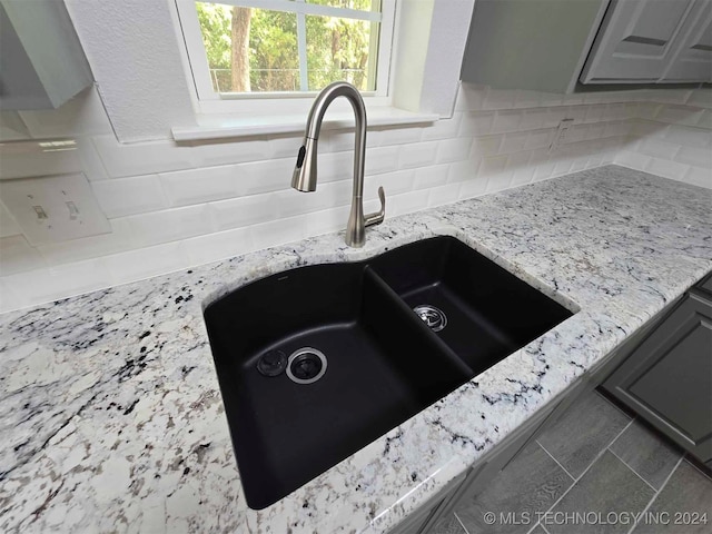 room details with gray cabinetry, backsplash, light stone countertops, and sink