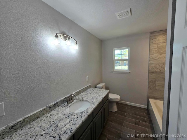 bathroom with vanity, a textured ceiling, a bathtub, and toilet