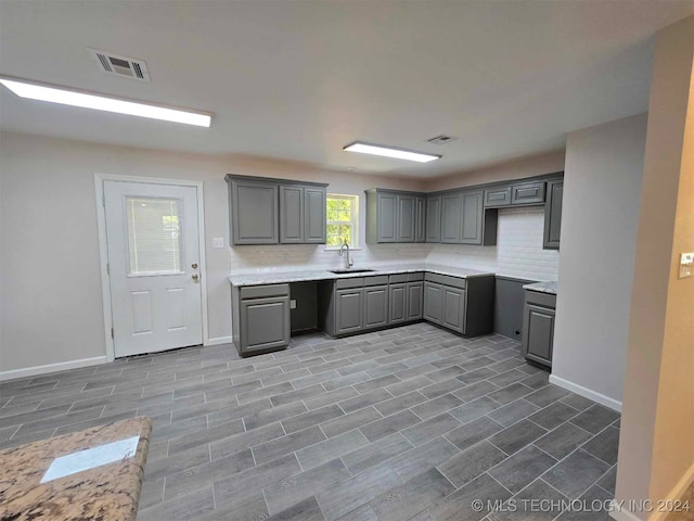 kitchen featuring wood-type flooring, gray cabinets, sink, and decorative backsplash