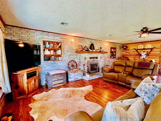 living room featuring brick wall, a brick fireplace, a textured ceiling, ceiling fan, and hardwood / wood-style flooring