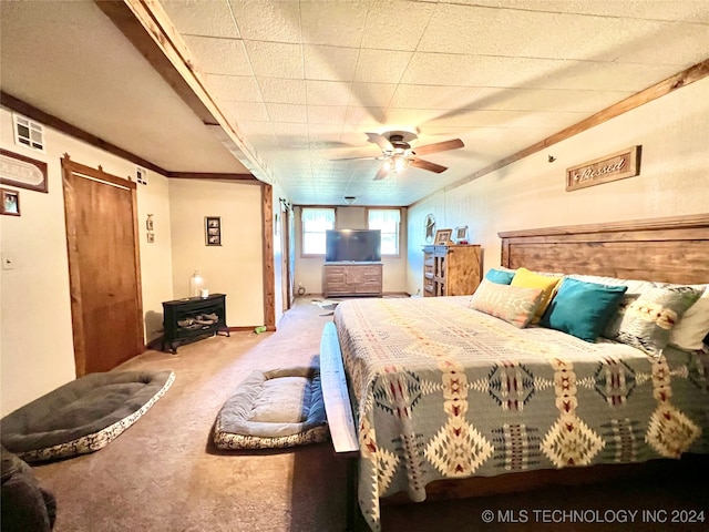 carpeted bedroom featuring ceiling fan, crown molding, and a wood stove