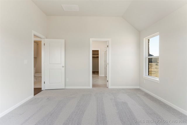 unfurnished bedroom featuring a walk in closet, a closet, light colored carpet, and lofted ceiling