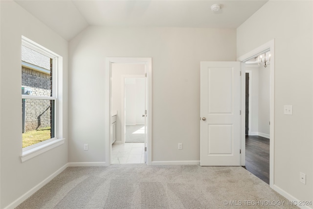 unfurnished bedroom with light carpet, vaulted ceiling, and a notable chandelier