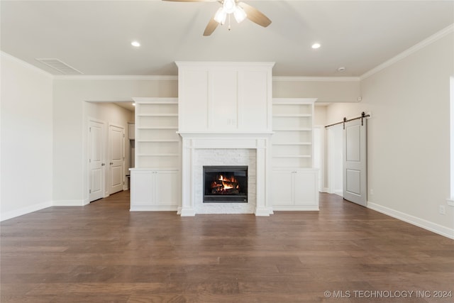 unfurnished living room with a barn door, dark hardwood / wood-style floors, ceiling fan, and ornamental molding