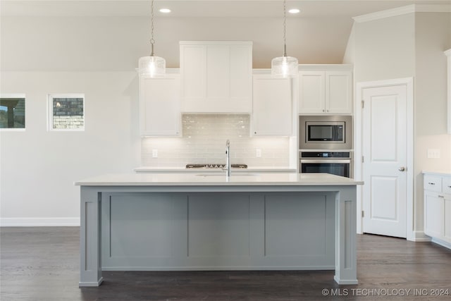 kitchen featuring appliances with stainless steel finishes, dark hardwood / wood-style flooring, pendant lighting, white cabinets, and an island with sink