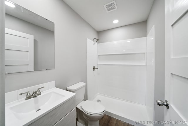 bathroom with hardwood / wood-style flooring, a shower, vanity, and toilet