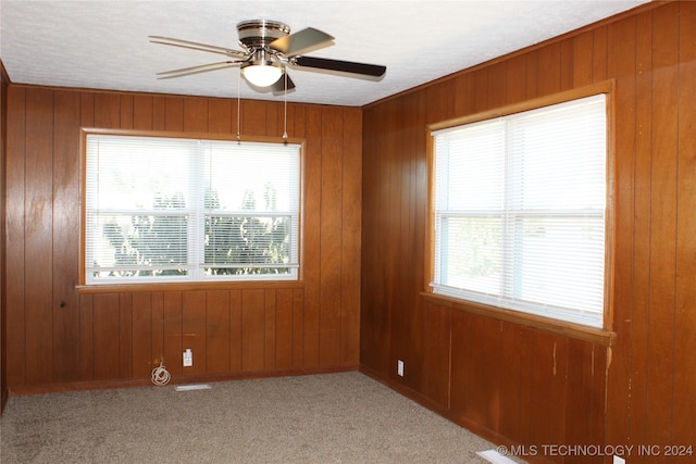 empty room featuring light carpet, wooden walls, and ceiling fan