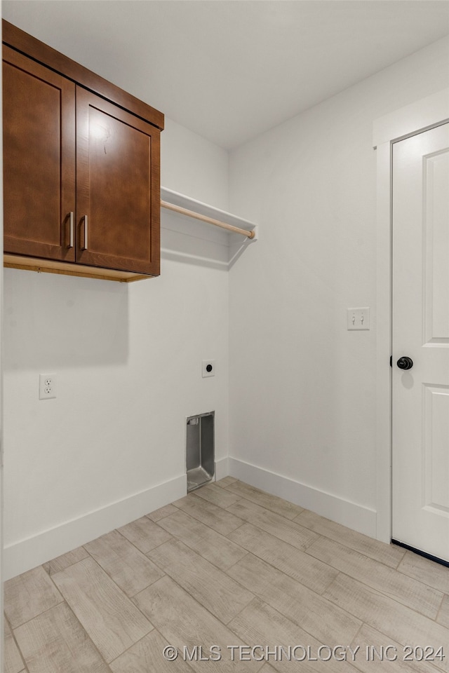 clothes washing area featuring electric dryer hookup, light hardwood / wood-style floors, and cabinets