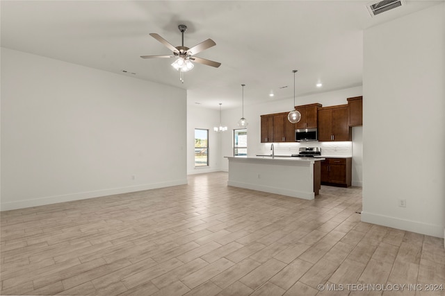 kitchen with appliances with stainless steel finishes, sink, hanging light fixtures, light hardwood / wood-style flooring, and a center island with sink