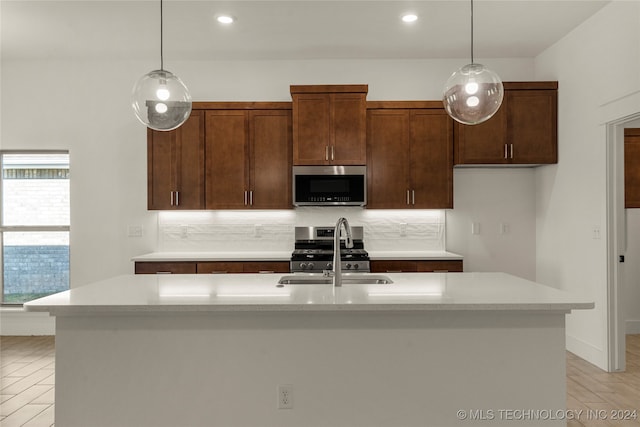 kitchen featuring stainless steel appliances, light hardwood / wood-style flooring, pendant lighting, and a kitchen island with sink