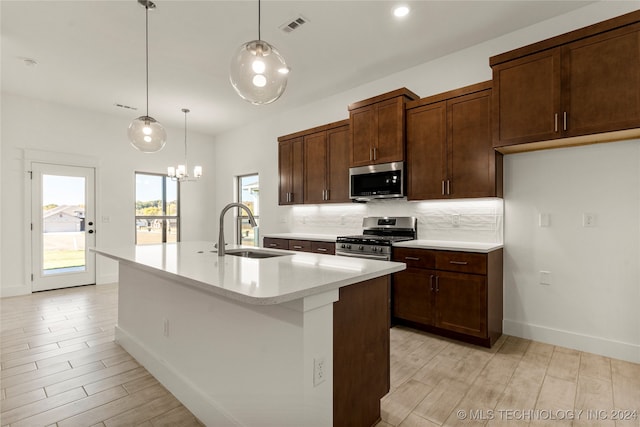 kitchen featuring decorative backsplash, a center island with sink, appliances with stainless steel finishes, sink, and decorative light fixtures