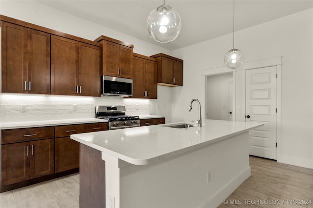 kitchen with light hardwood / wood-style flooring, hanging light fixtures, stainless steel appliances, a center island with sink, and sink