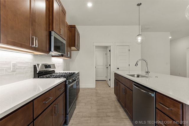 kitchen with tasteful backsplash, hanging light fixtures, appliances with stainless steel finishes, light hardwood / wood-style floors, and sink