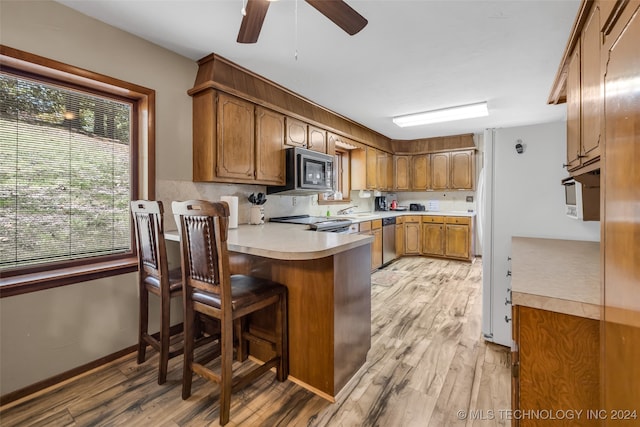 kitchen with kitchen peninsula, stainless steel appliances, light wood-type flooring, a kitchen bar, and ceiling fan