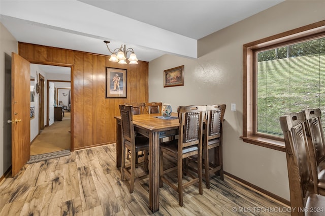 dining room featuring a healthy amount of sunlight, light hardwood / wood-style floors, wood walls, and an inviting chandelier