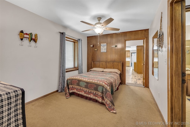 bedroom featuring ceiling fan, light colored carpet, wooden walls, and ensuite bath