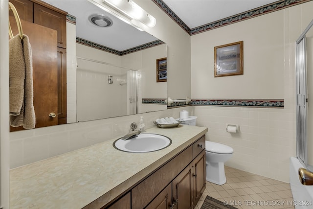 bathroom with vanity, toilet, a shower, tile walls, and tile patterned flooring