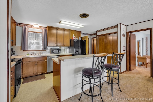 kitchen with a textured ceiling, black appliances, a breakfast bar area, and light carpet