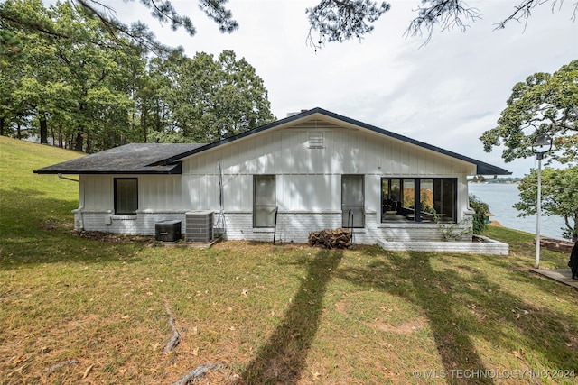 back of property with cooling unit, a water view, and a yard