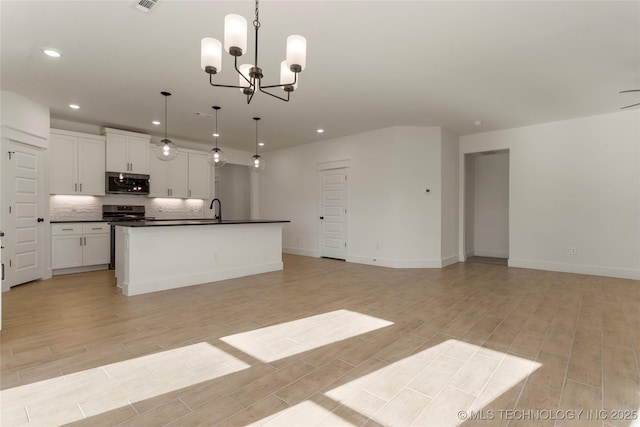 kitchen with pendant lighting, appliances with stainless steel finishes, white cabinetry, an inviting chandelier, and a kitchen island with sink