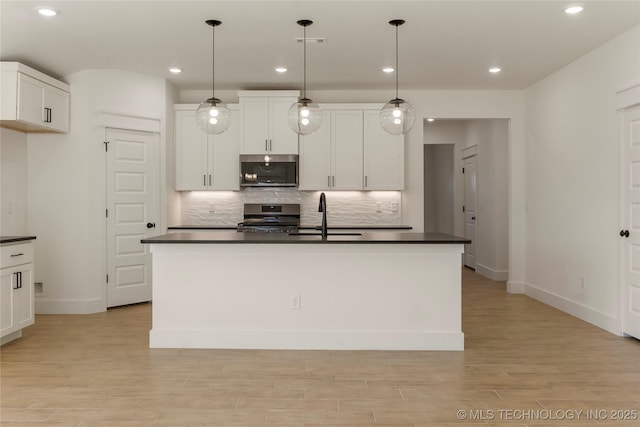 kitchen featuring pendant lighting, stainless steel stove, sink, white cabinetry, and a kitchen island with sink