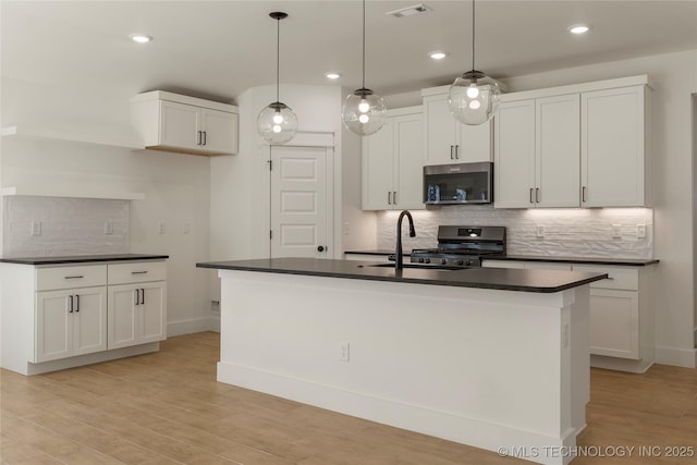 kitchen with light wood-type flooring, pendant lighting, white cabinets, and an island with sink