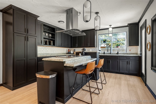 kitchen with light stone counters, tasteful backsplash, a kitchen island, island exhaust hood, and light hardwood / wood-style floors