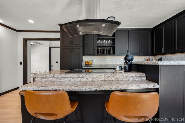 kitchen with tasteful backsplash, black electric cooktop, a breakfast bar area, light stone countertops, and light hardwood / wood-style floors