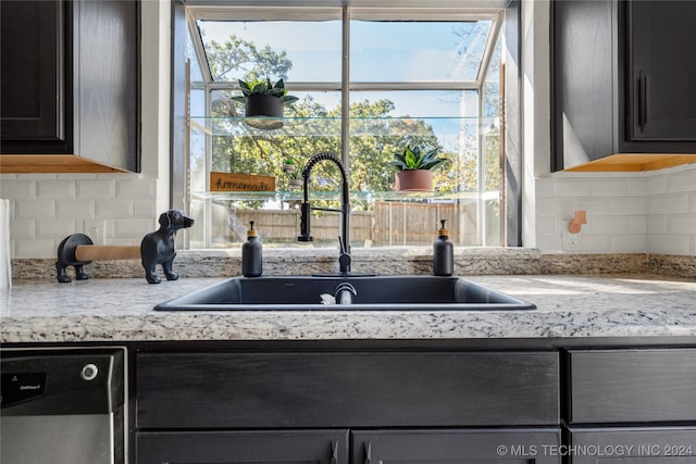 interior details with backsplash, light stone counters, sink, and stainless steel dishwasher