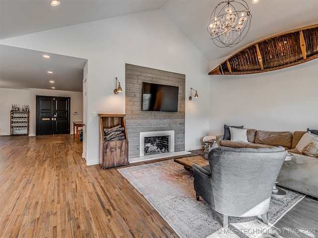 living room with high vaulted ceiling, wood-type flooring, a chandelier, and a fireplace