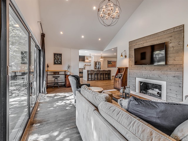 living room with wood-type flooring, an inviting chandelier, high vaulted ceiling, and a large fireplace