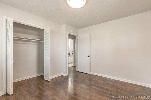 unfurnished bedroom featuring a textured ceiling, a closet, and dark wood-type flooring