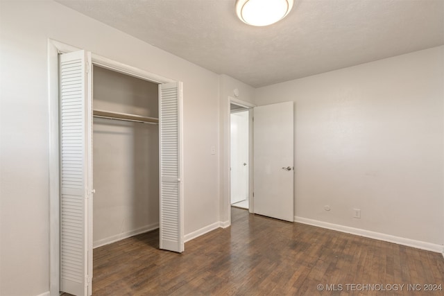 unfurnished bedroom with a textured ceiling, a closet, and dark wood-type flooring