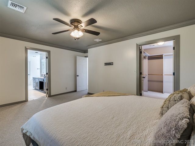 carpeted bedroom with a spacious closet, a closet, a textured ceiling, crown molding, and ceiling fan