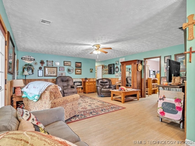 living room with a textured ceiling, ceiling fan, and light hardwood / wood-style flooring