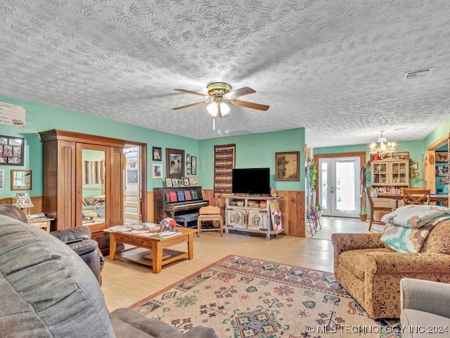 living room with ceiling fan with notable chandelier, wooden walls, a textured ceiling, and light hardwood / wood-style flooring