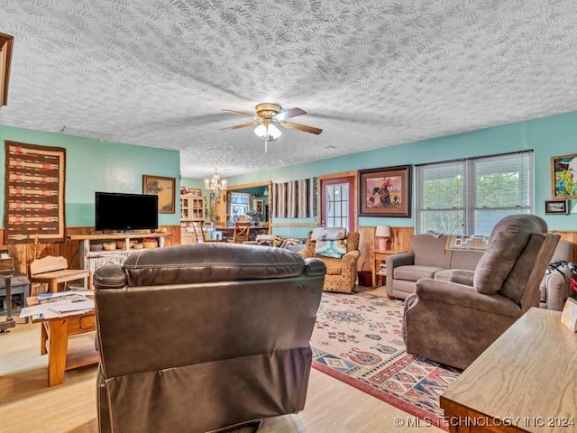 living room featuring wooden walls, light hardwood / wood-style floors, ceiling fan, and a textured ceiling