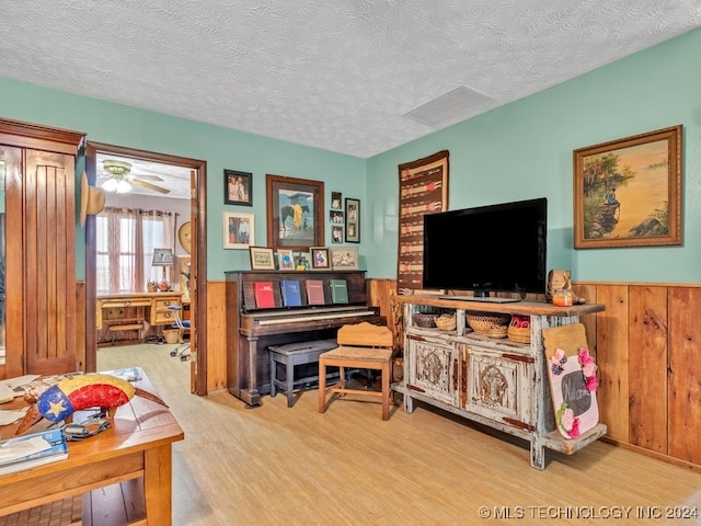 interior space featuring a textured ceiling, wooden walls, hardwood / wood-style floors, and ceiling fan