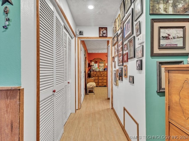 corridor with a textured ceiling and light hardwood / wood-style flooring