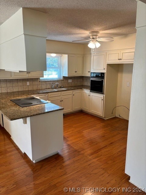 kitchen with tasteful backsplash, white cabinets, kitchen peninsula, black appliances, and dark hardwood / wood-style flooring