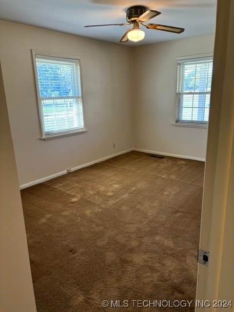 unfurnished room featuring dark colored carpet, ceiling fan, and a wealth of natural light