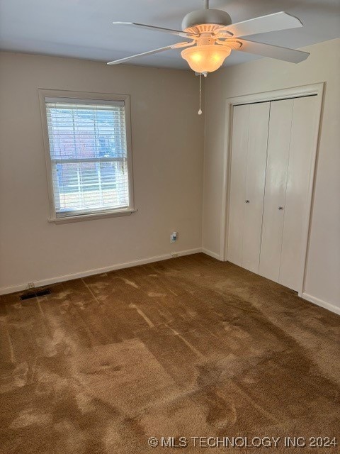 unfurnished bedroom with ceiling fan, a closet, and dark colored carpet